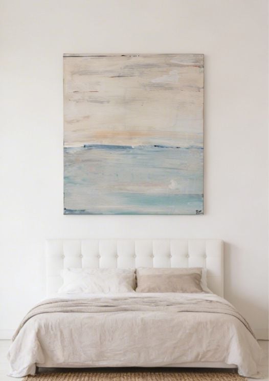 Minimalist bedroom with a white tufted headboard bed and beige bedding, topped with an abstract landscape painting in soft blues and neutrals